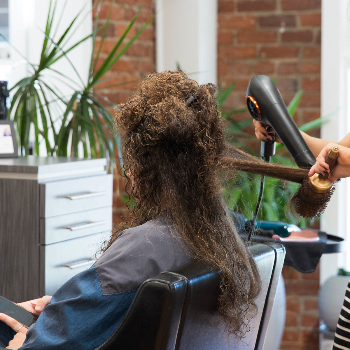Hyde Salon Vista guest having long curly hair blown out with a round brush